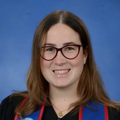 Young woman with light brown hair and brown glasses smiling against blue background